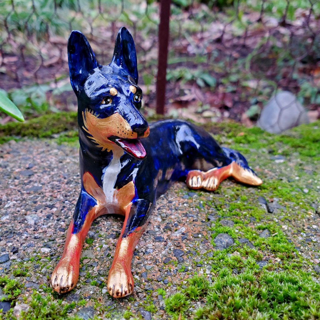 Photo of a small dog figurine, painted black and gold with red and blue undertones. 
